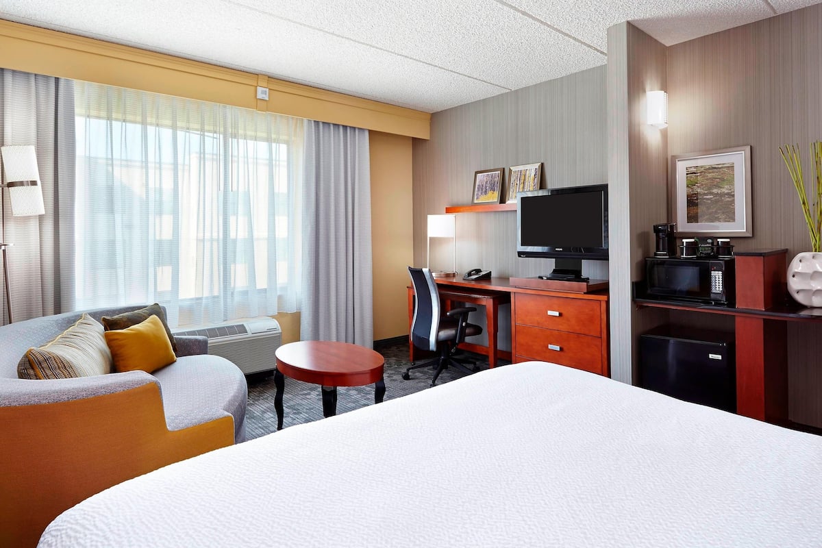 Una habitación de hotel con una cama grande, un escritorio, una silla, una mesita, un televisor, una cafetera y un refrigerador.