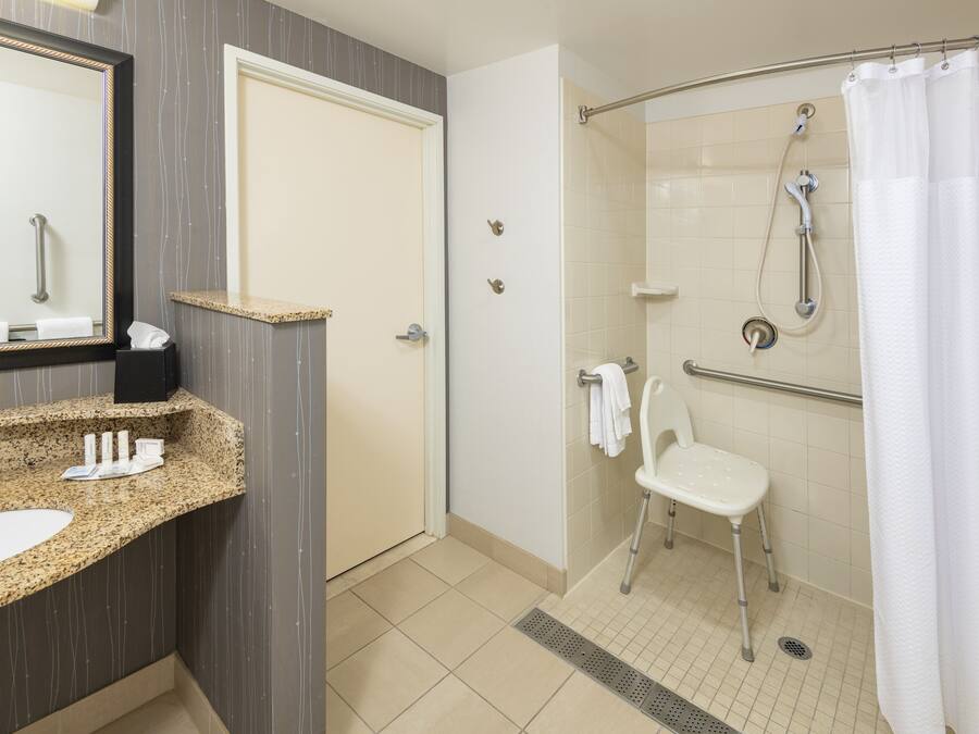 A bathroom with a sink, mirror, shower, and a wheelchair-accessible chair.