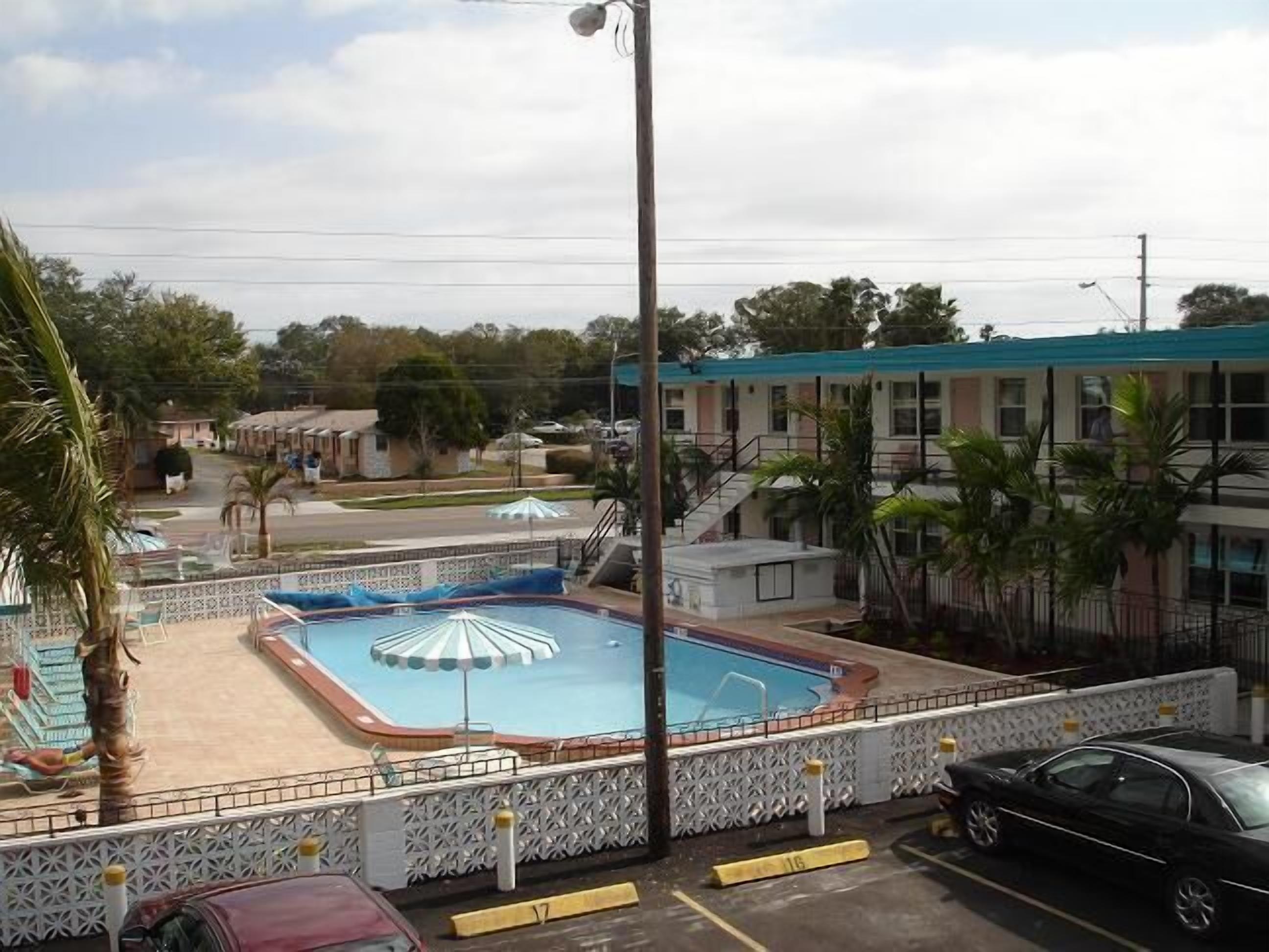 A swimming pool with a covered area, a parking lot, and a building with a blue roof.