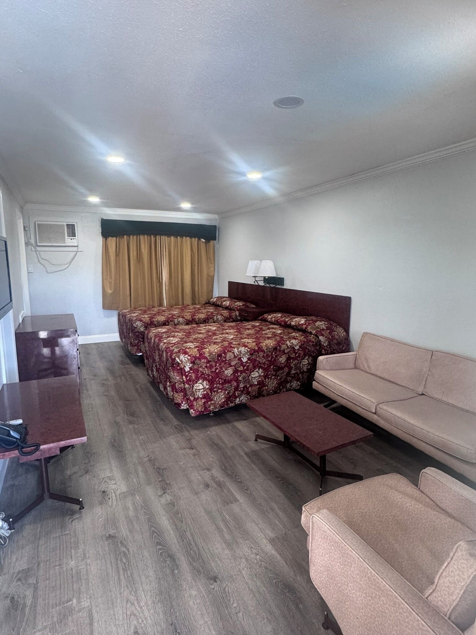 A hotel room with a bed, a sofa, a desk, and an air conditioning unit.