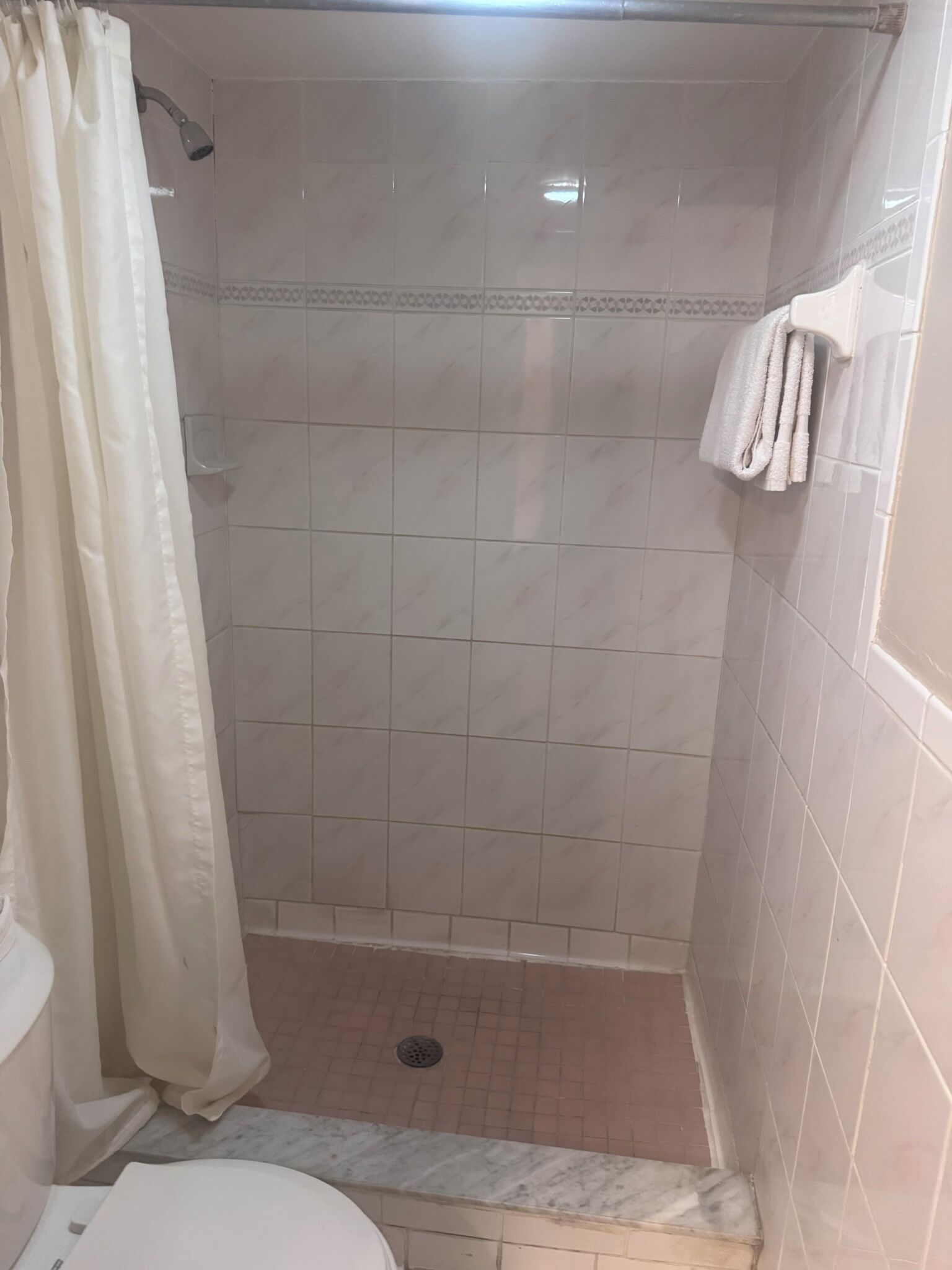 Un petit espace de douche carrelé, équipé d’un pommeau de douche, d’un drain et d’un porte-serviettes.