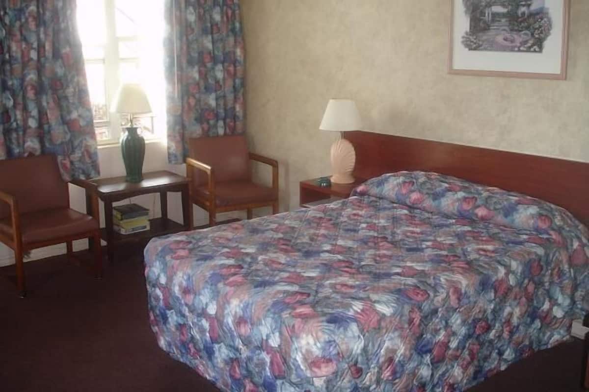 Habitación de hotel con una cama, dos sillas, una mesita, una lámpara y un cuadro en la pared.