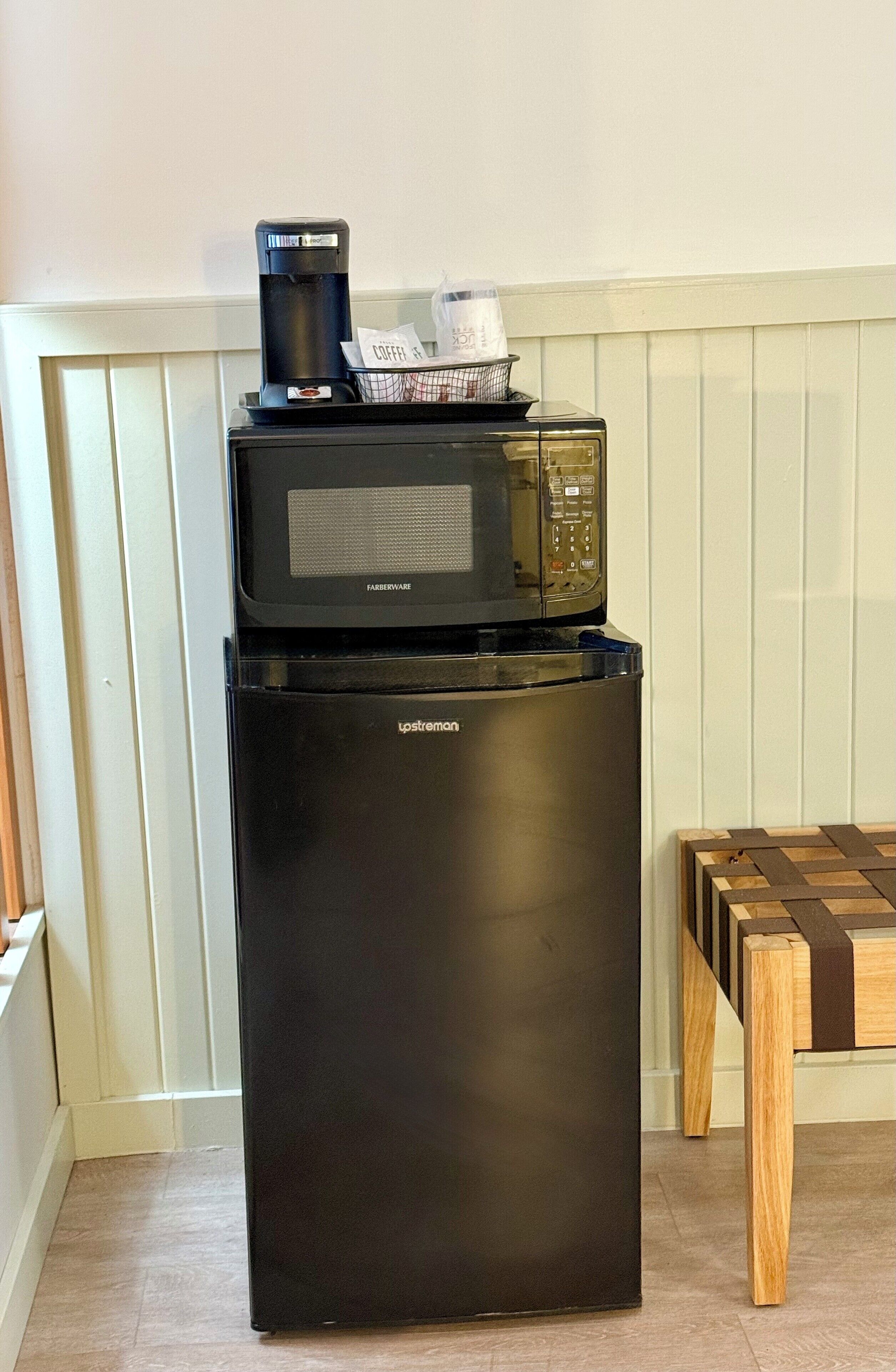 Ein schwarzer Kühlschrank mit einer Mikrowelle darüber, einer Kaffeemaschine und einer Plastiktüte mit einem Kassenbon.