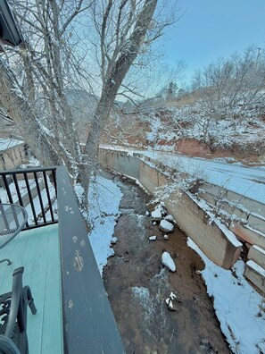 A snow-covered outdoor area with a concrete pathway, a metal railing, and a small stream. - Pikes Peak Inn (Manitou Springs)