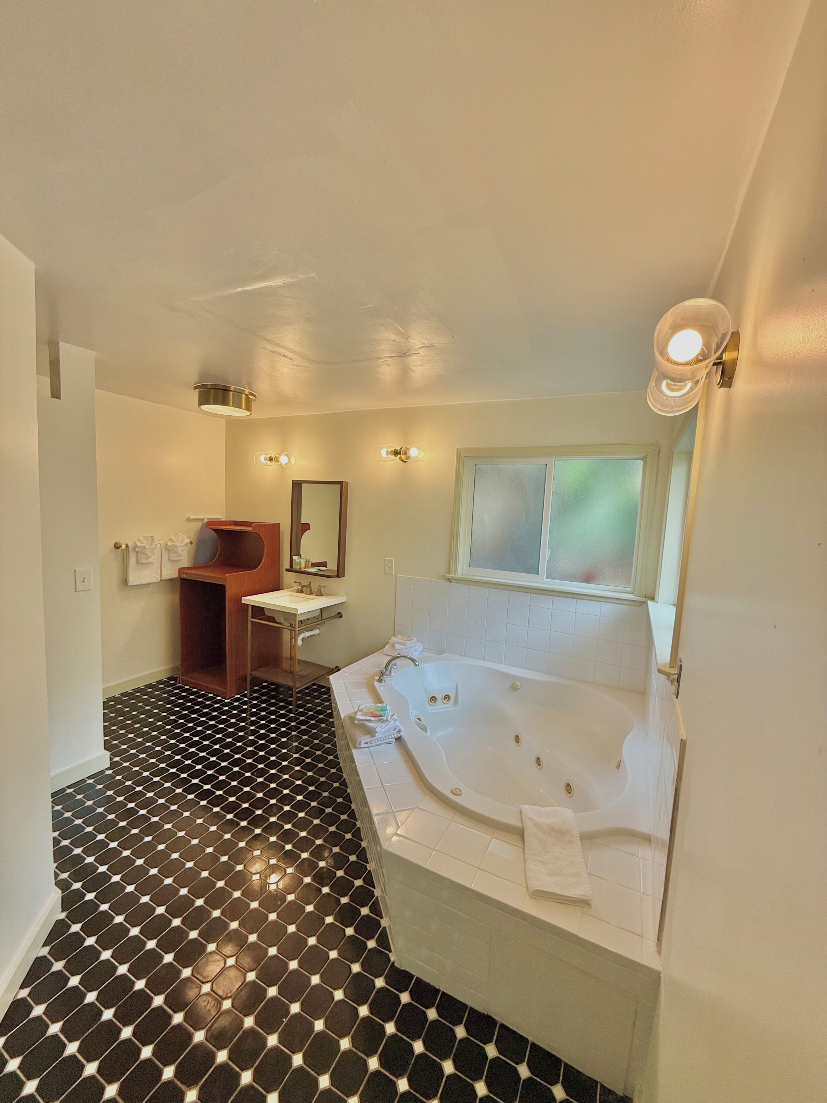 A bathroom with a large bathtub, a sink, a mirror, and a window.