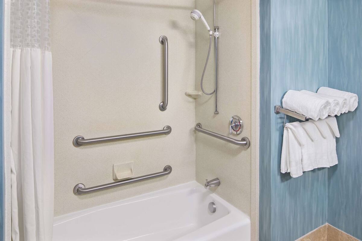 A bathroom with a bathtub, grab bars, a showerhead, and a towel rack.
