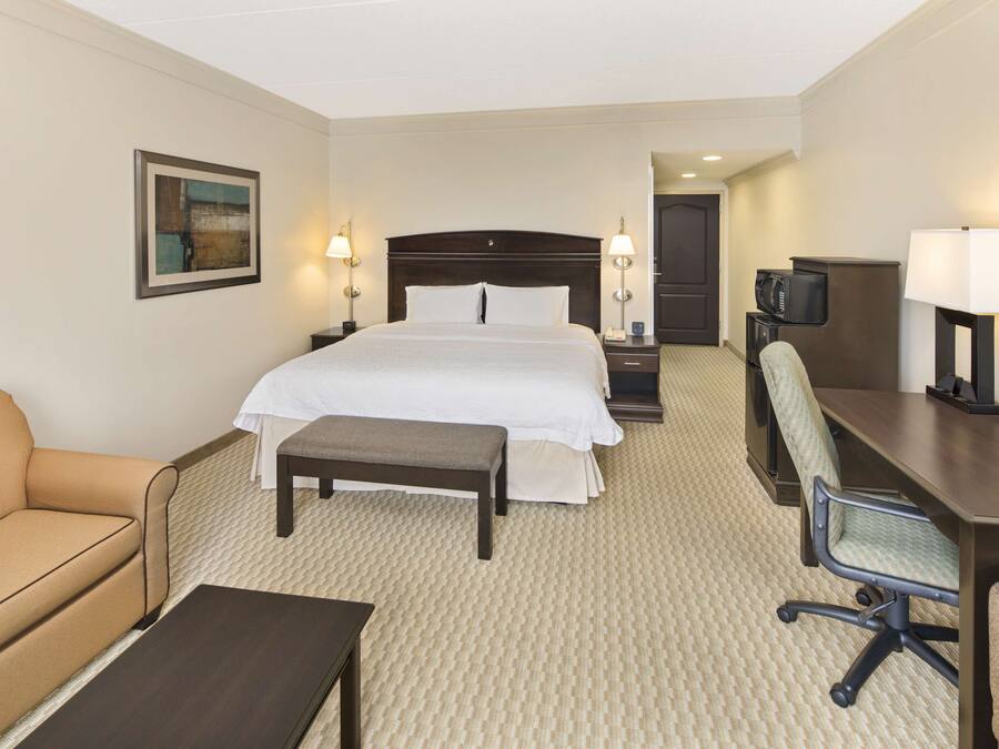 A hotel room with a bed, a desk, a chair, a sofa, and a television.