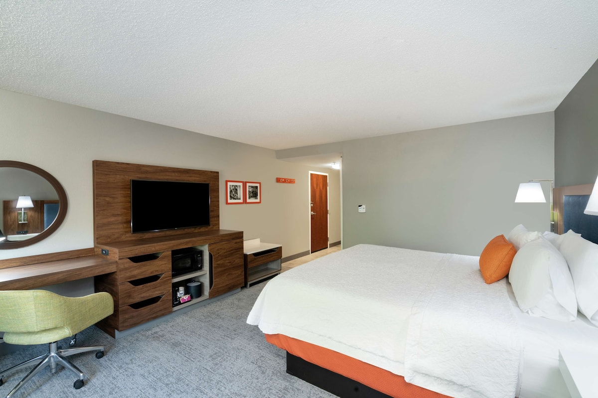 A hotel room with a bed, a desk with a chair, a television, and a mirror.