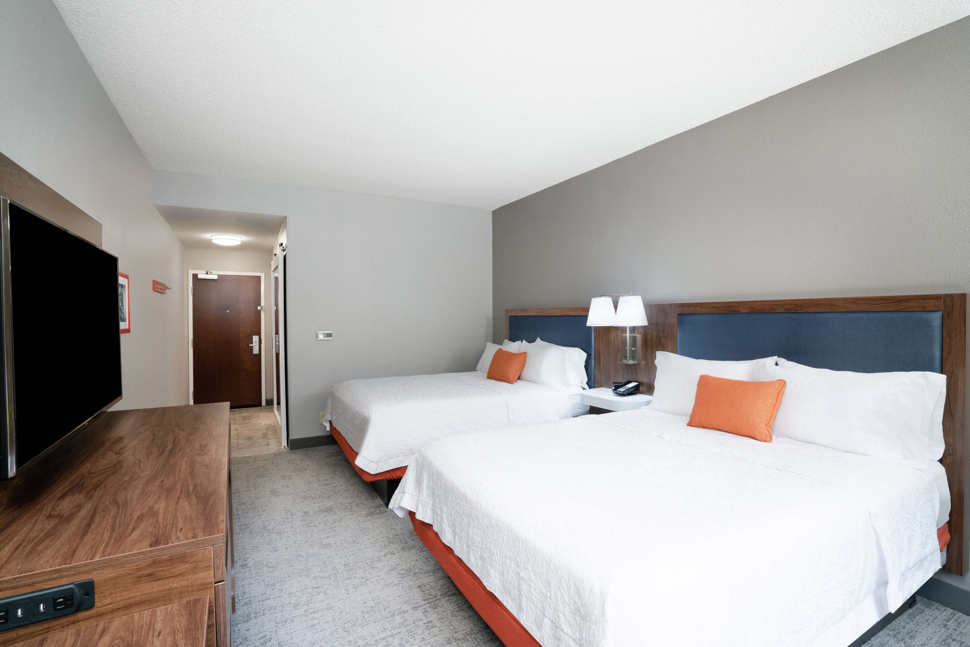 A hotel room with two beds, a TV, and a desk.