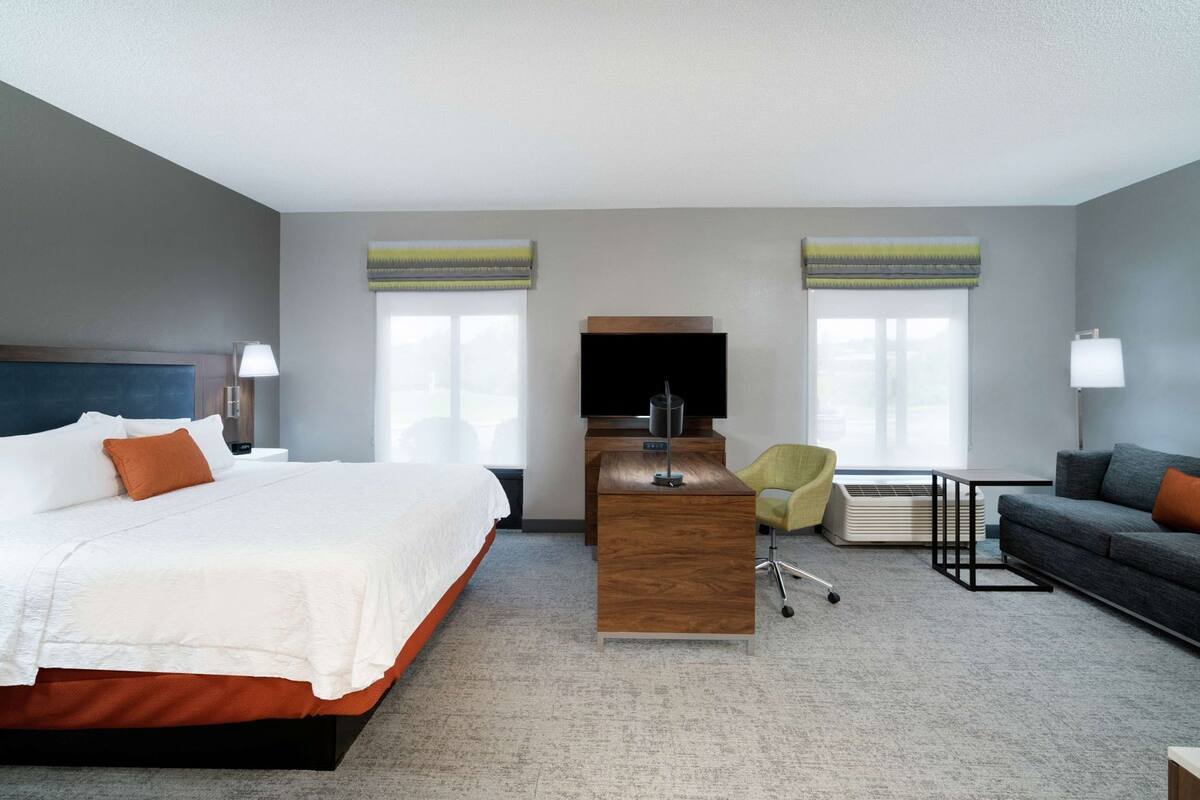 A hotel room with a bed, desk, TV, and seating area.