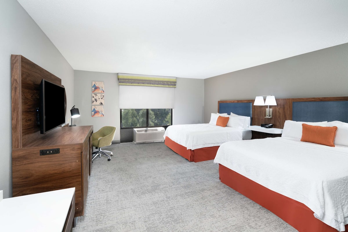 A hotel room with two beds, a desk, a TV, and a window with a view.