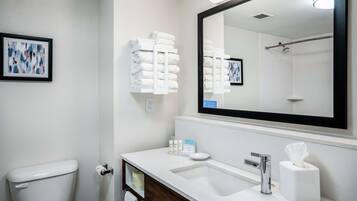 Un bany modern amb un lavabo blanc, un mirall gran i un vàter. Hi ha tovalloles i productes de tocador a la superfície.