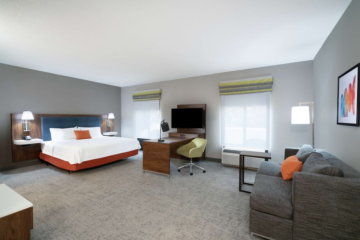 A hotel room with a bed, desk, chair, and a sofa.