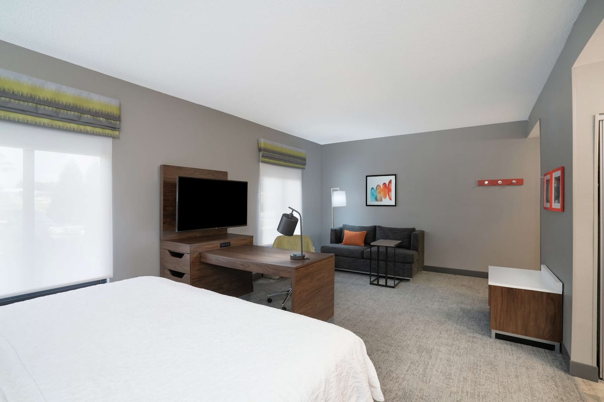 A modern hotel room with a large bed, a desk, a television, a sofa, and a small table.