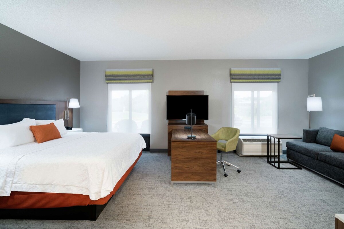 A hotel room with a bed, desk, TV, and seating area.