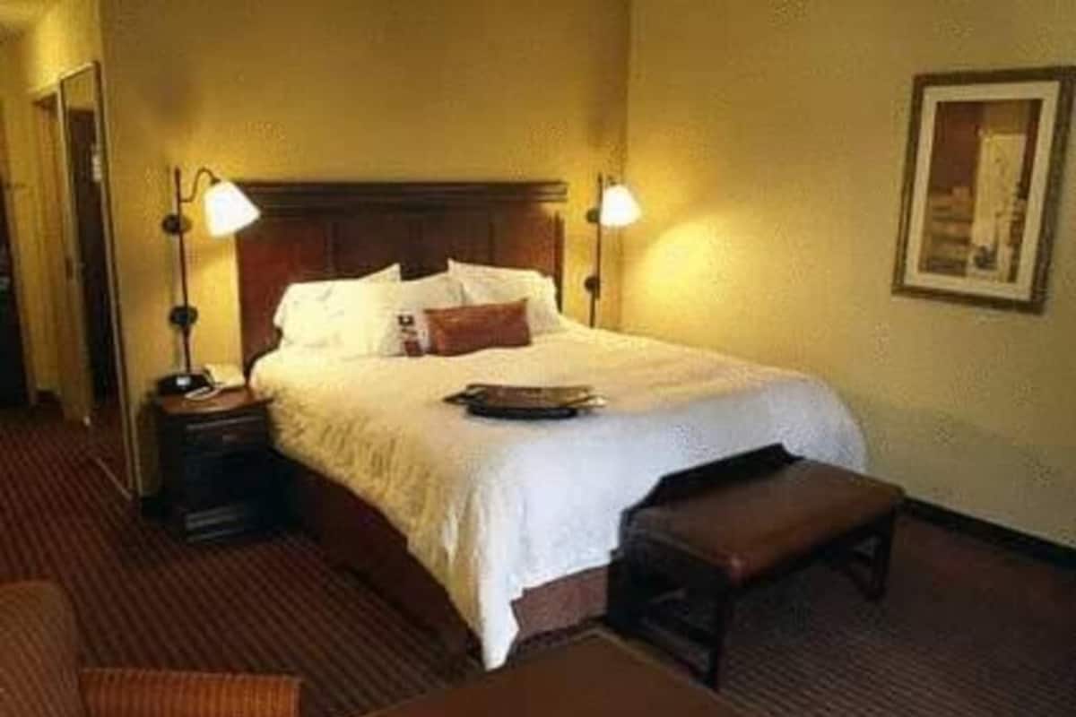 A hotel room with a bed, bedside lamps, a nightstand, a bench, and a framed picture on the wall.