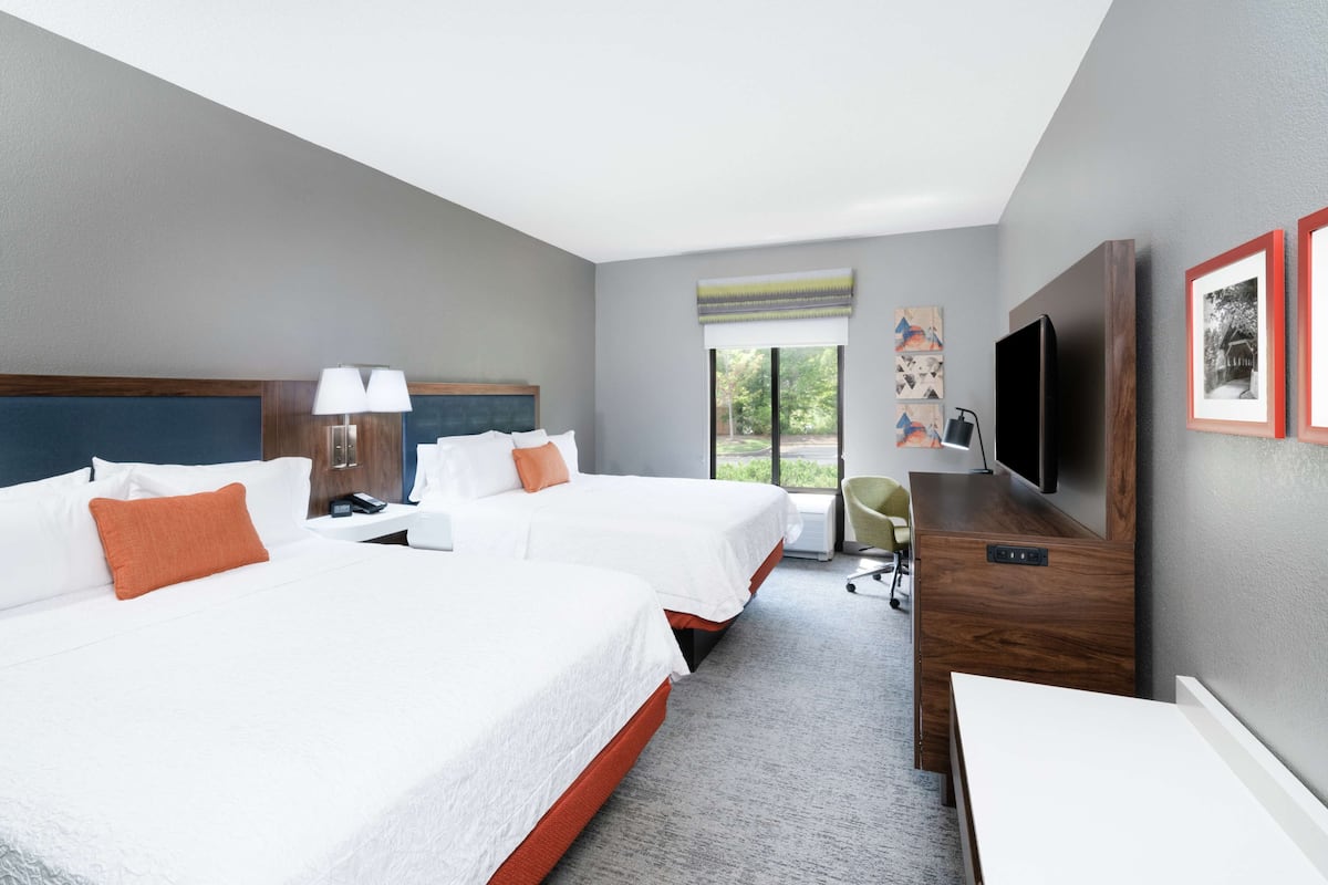 A hotel room with two beds, a desk, a chair, a television, and artwork on the walls.