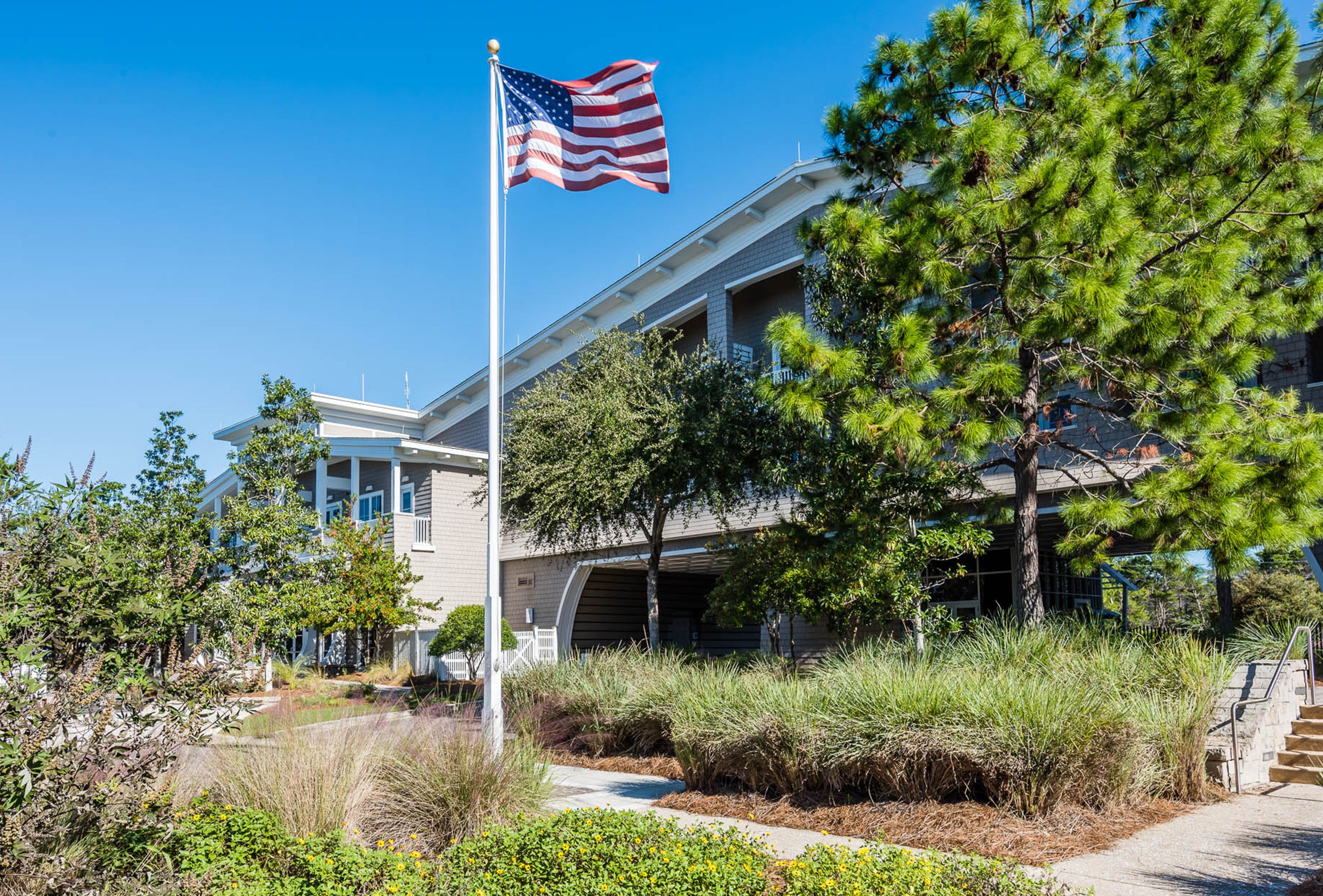 A building with a flagpole, a staircase, and a well-maintained garden with various plants.