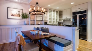 A modern kitchen with white cabinetry, a dining table with a bench, and a built-in oven. - WaterSound Inn (Santa Rosa Beach)