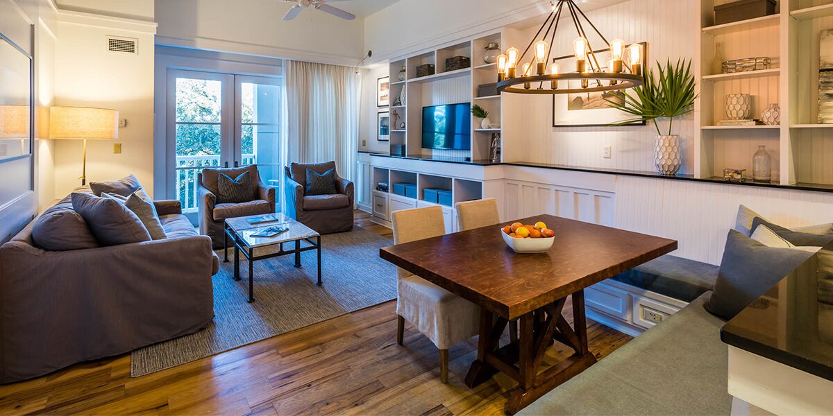 A modern living room with a wooden dining table, sofas, and a TV in the background.