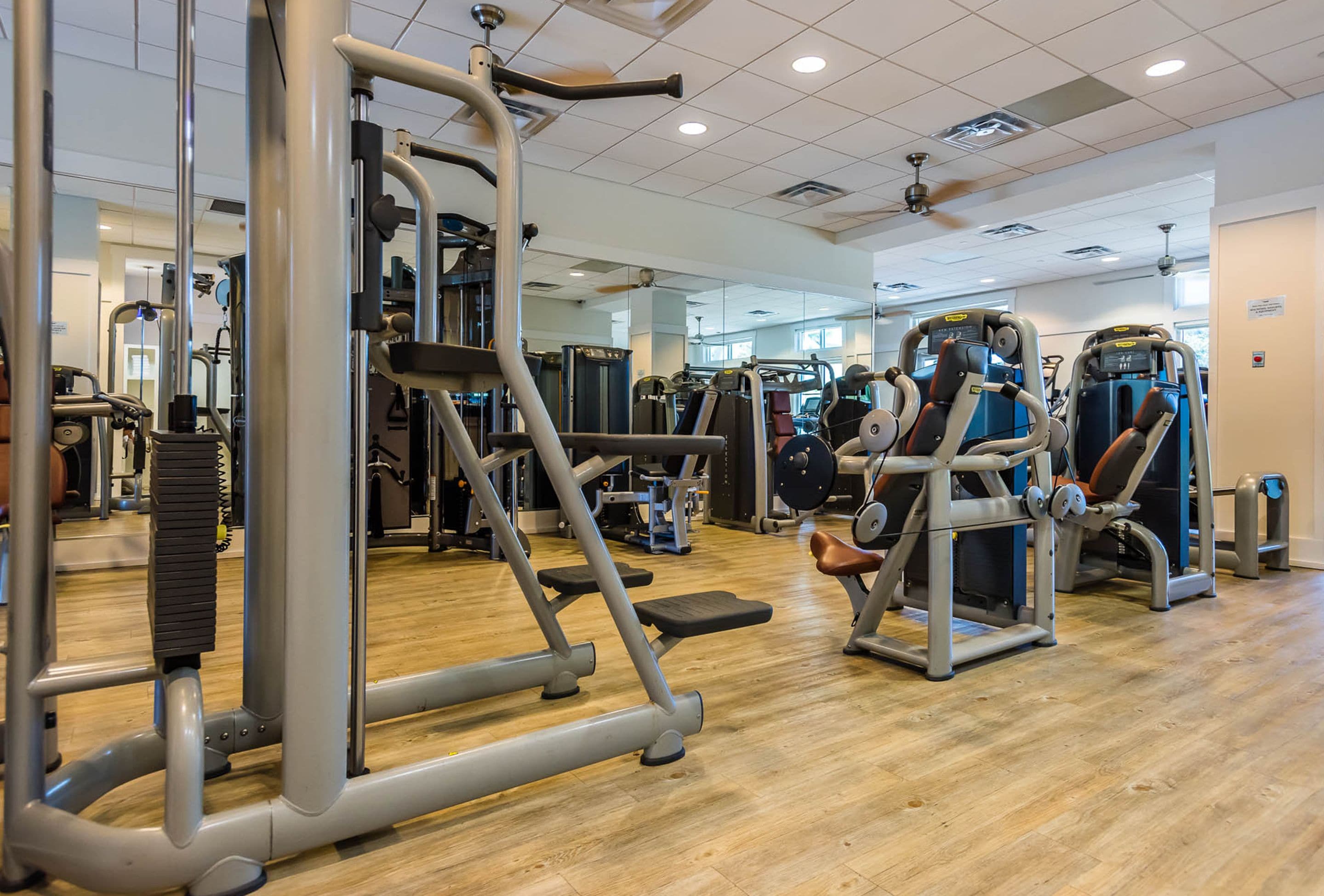 Ein Fitnessstudio mit verschiedenen Trainingsgeräten, Holzboden und einer Spiegelwand.