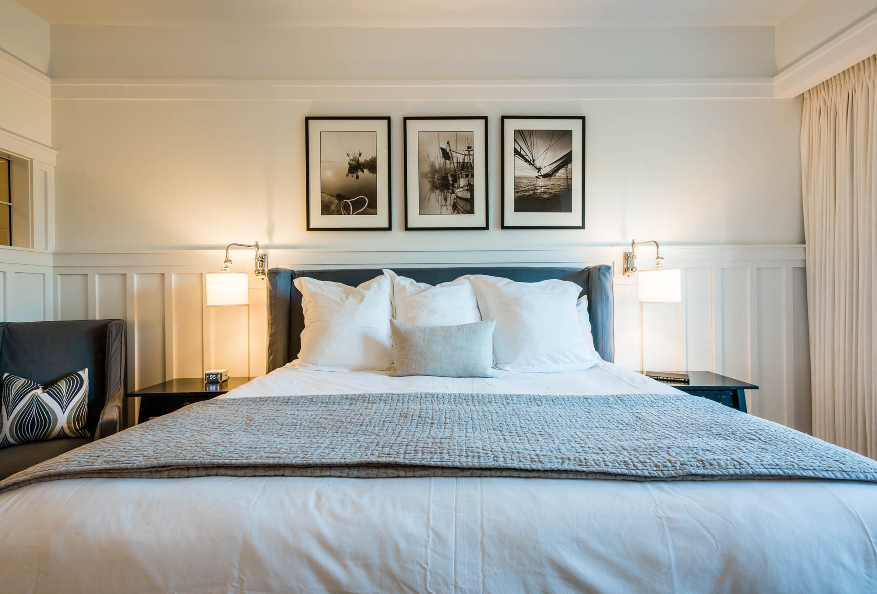 A neatly made bed with a blue headboard, two bedside tables with lamps, and three framed pictures on the wall.