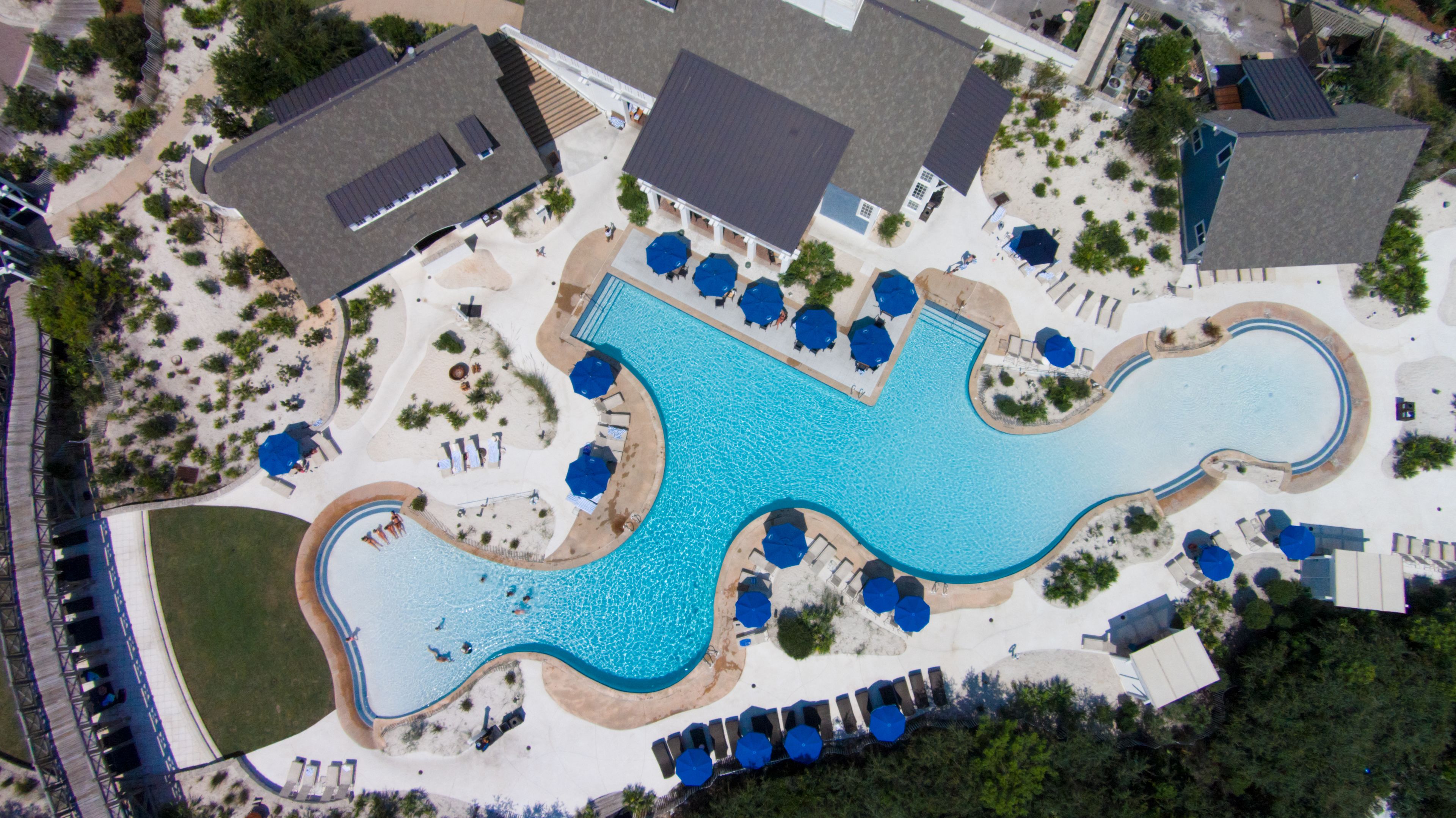 An aerial view of a resort with a large swimming pool, sun loungers, and a covered patio area.
