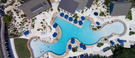 An aerial view of a resort with a large swimming pool, sun loungers, and a covered patio area.