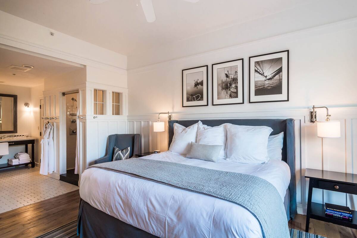 A hotel room with a large bed, a nightstand, a mirror, and framed pictures on the wall.