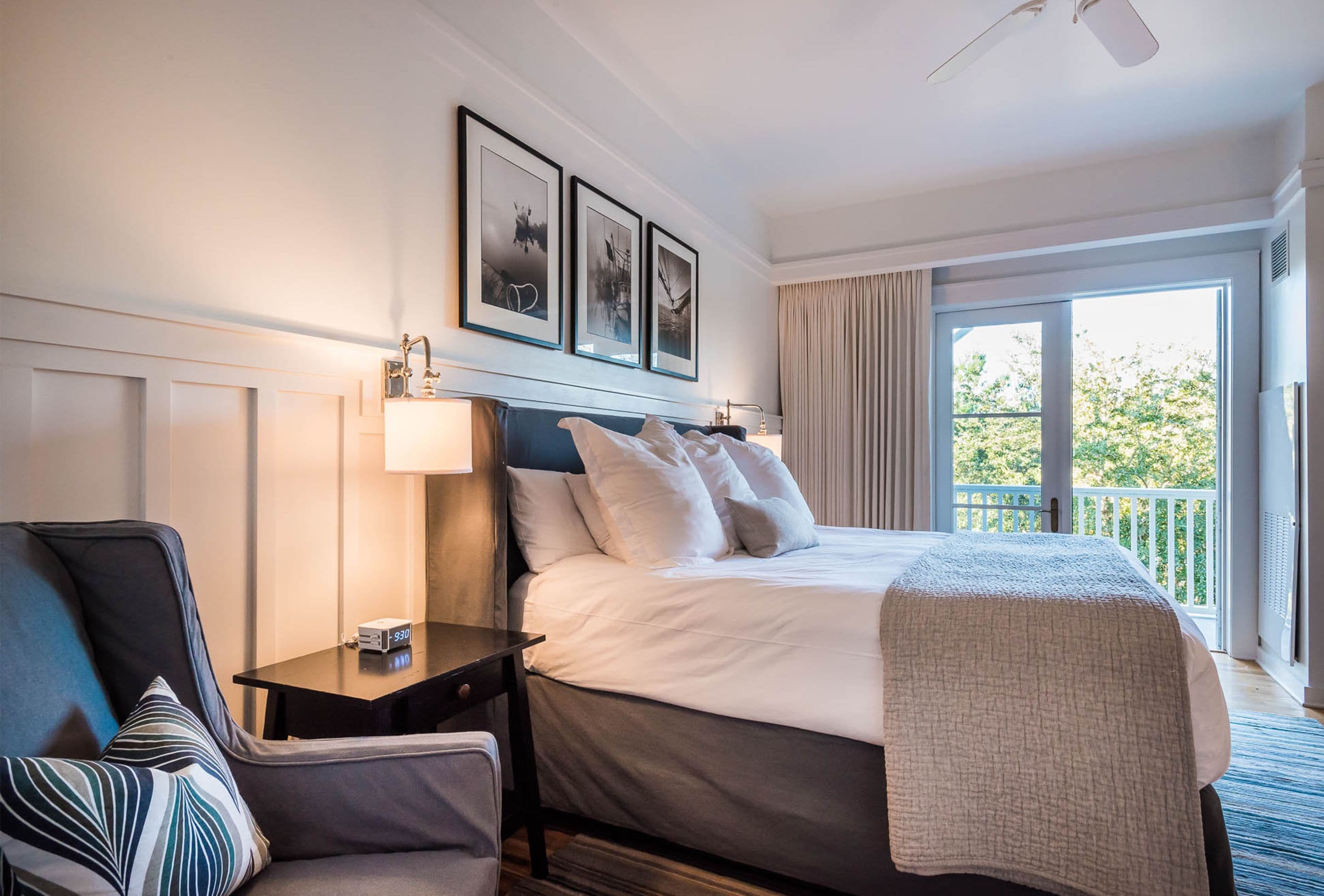 A hotel room with a bed, a desk, a chair, a lamp, and a balcony with a view.