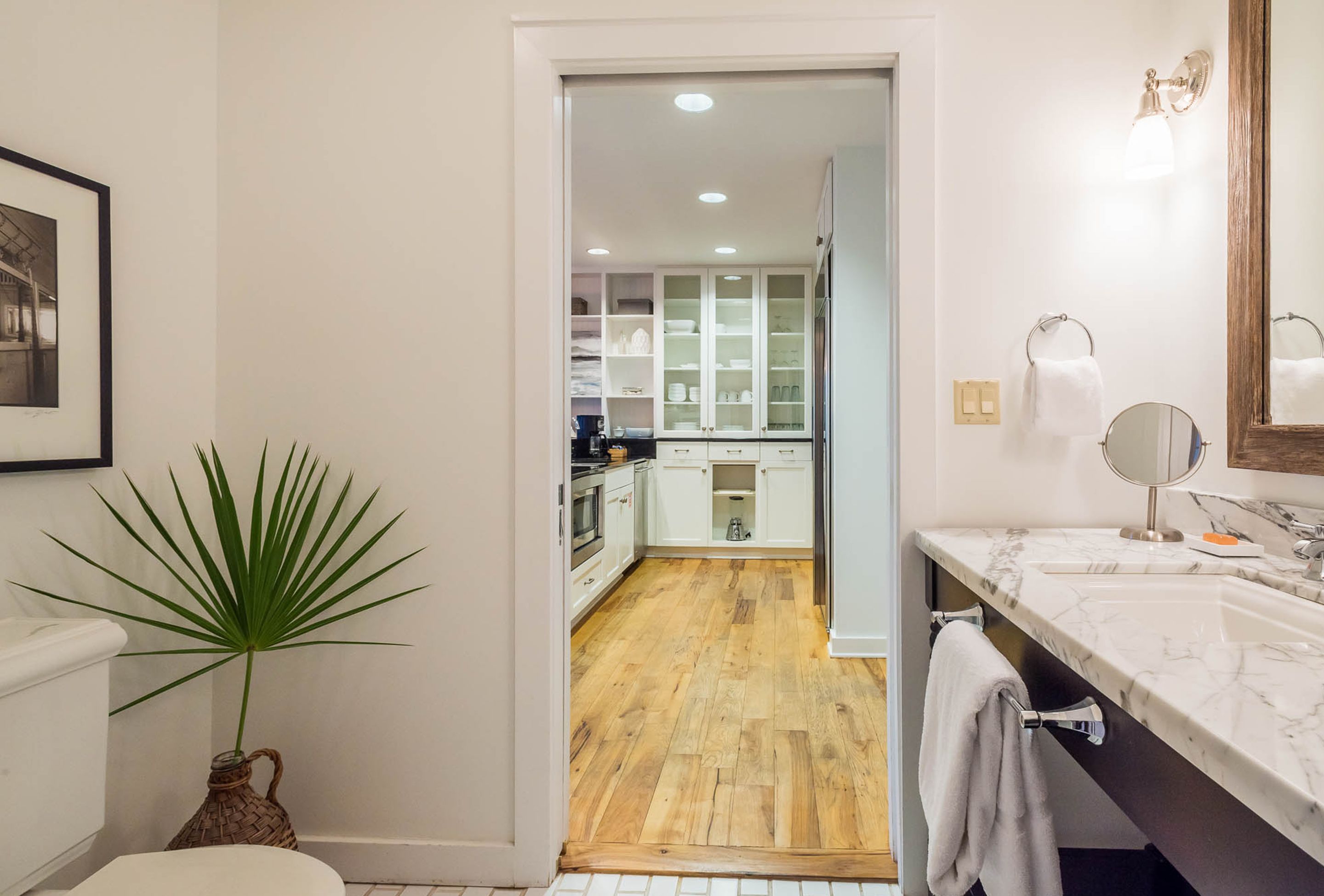 A modern bathroom with a marble sink, a mirror, and a potted plant.