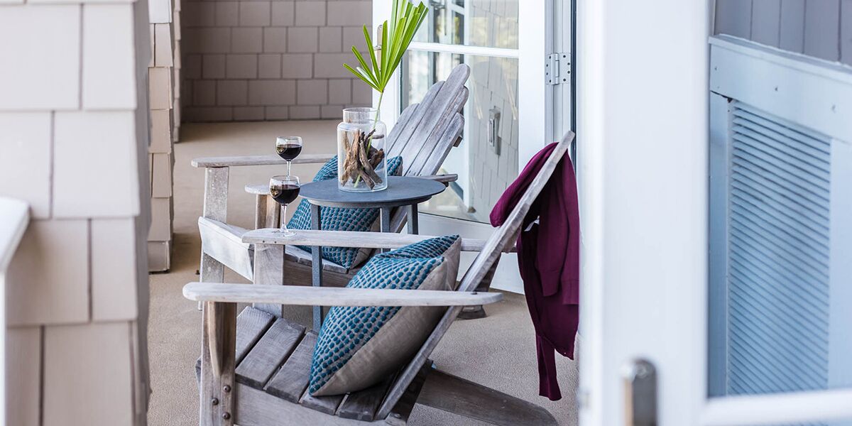 A balcony with a table, two chairs, a glass jar with a plant, and a red towel hanging on the wall.