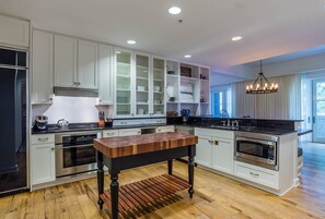 Une cuisine moderne avec des meubles blancs, un îlot central en bois, des appareils électroménagers en acier inoxydable et un lustre.