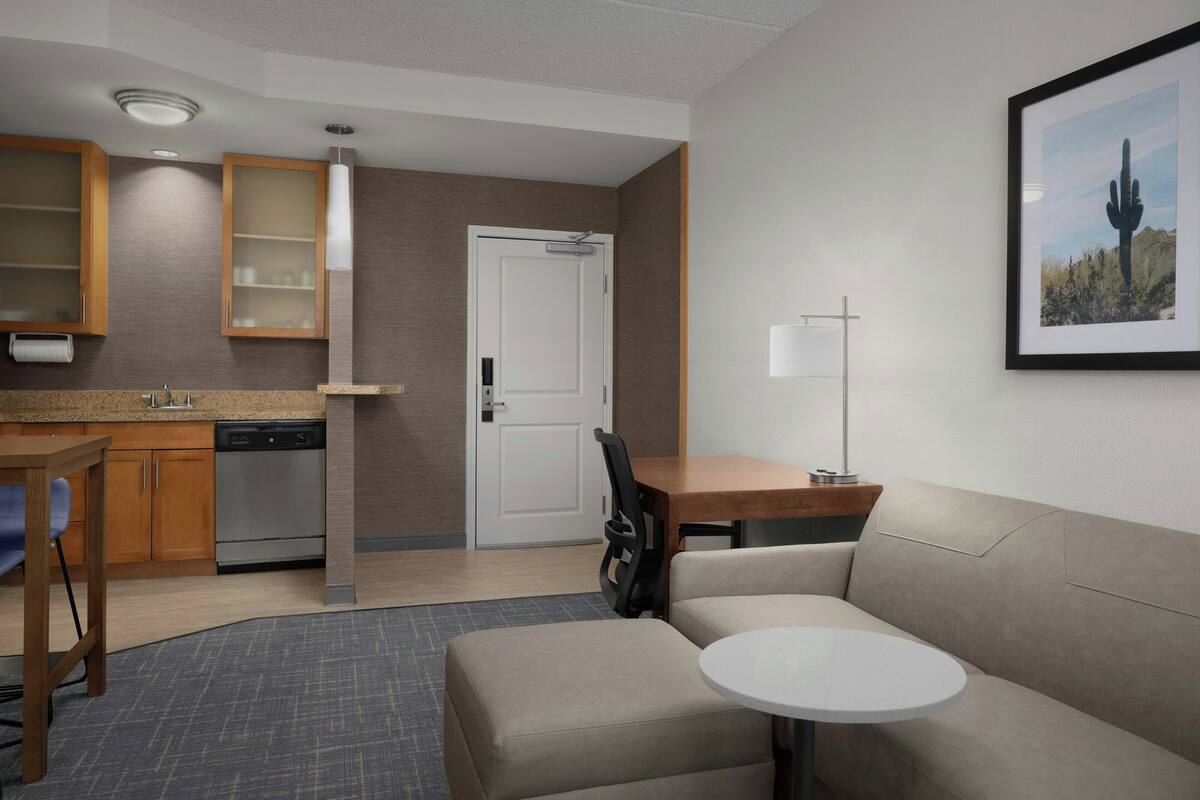 A compact hotel room with a kitchenette, a sofa, a small dining table, and a single chair.