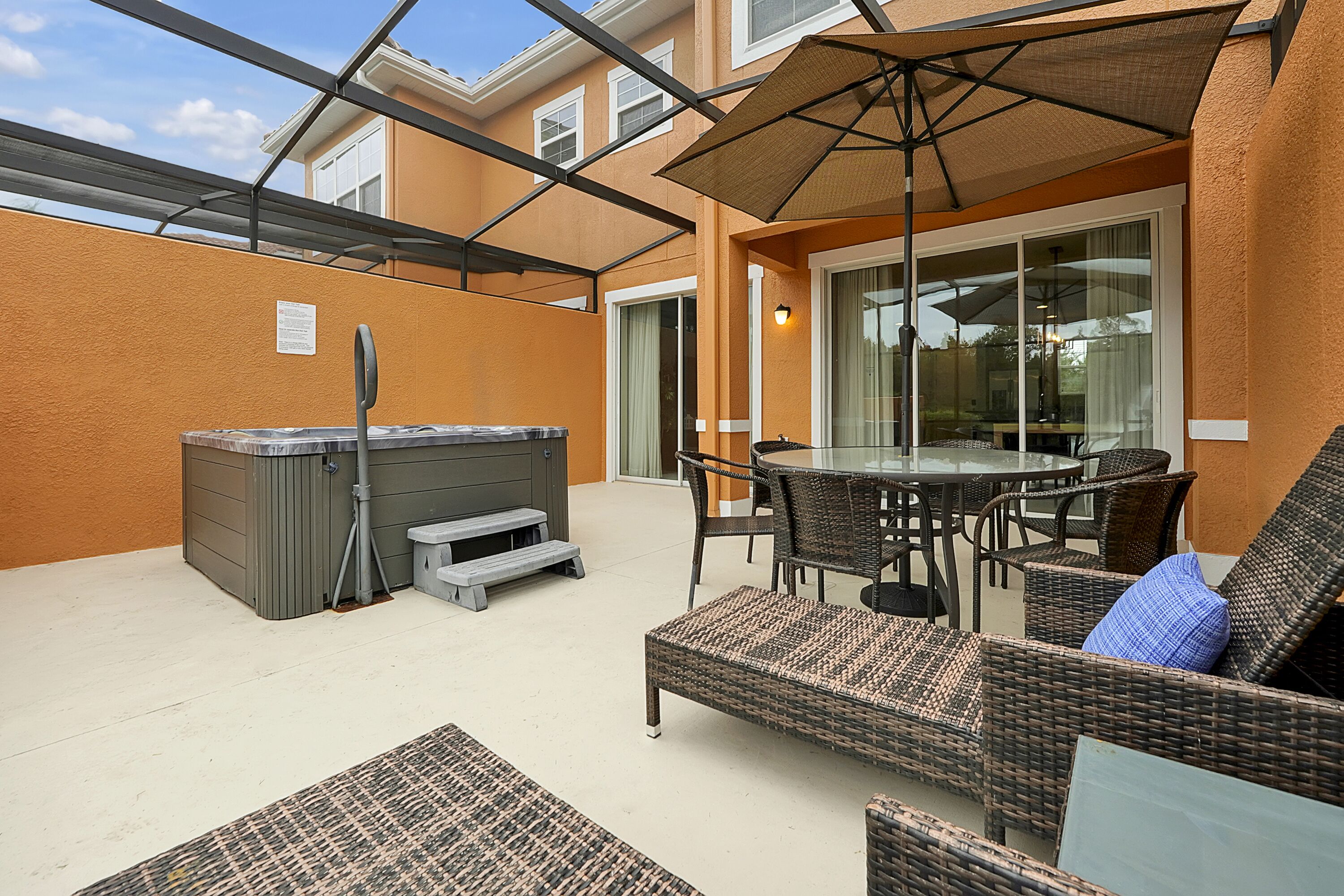 A covered patio with a hot tub, wicker furniture, and a glass door leading to an indoor area.