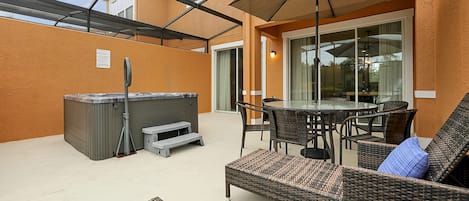 A covered patio with a hot tub, wicker furniture, and a glass door leading to an indoor area.