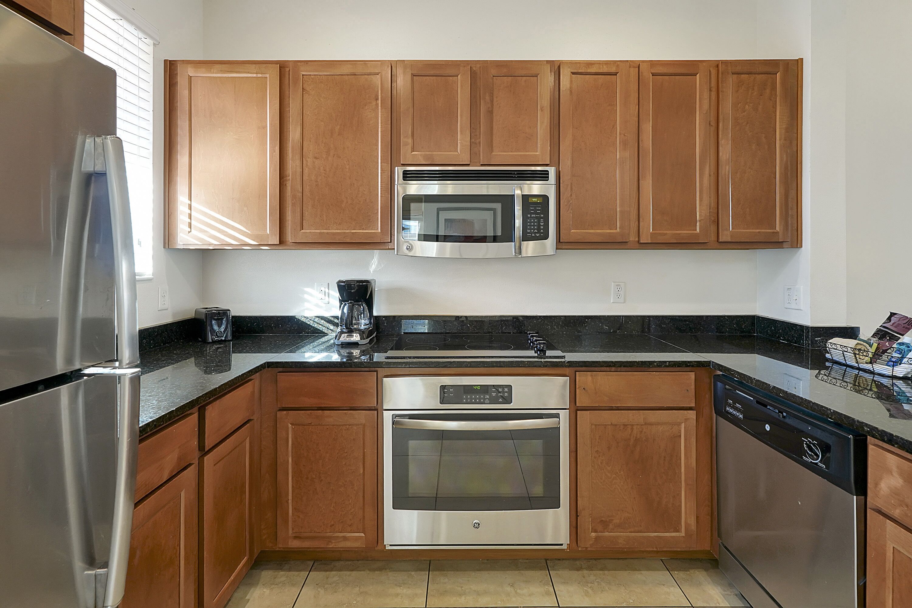 A kitchen with wooden cabinets, a stainless steel refrigerator, a microwave, an oven, and a dishwasher.