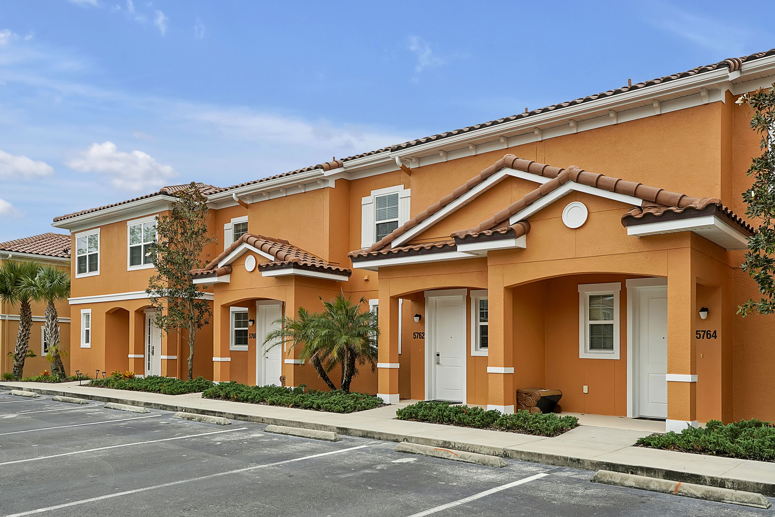 A row of townhouses with a uniform architectural style, featuring a consistent facade and a parking lot in front.