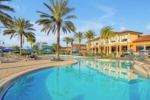 A swimming pool surrounded by palm trees and lounge chairs, with a building featuring balconies and large windows in the background. - Regal Oaks Resort Vacation Townhomes by IDILIQ (Kissimmee)