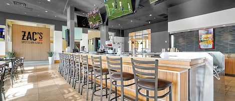 A sports bar and grill with multiple bar stools, a counter, and a TV screen displaying a sports game.