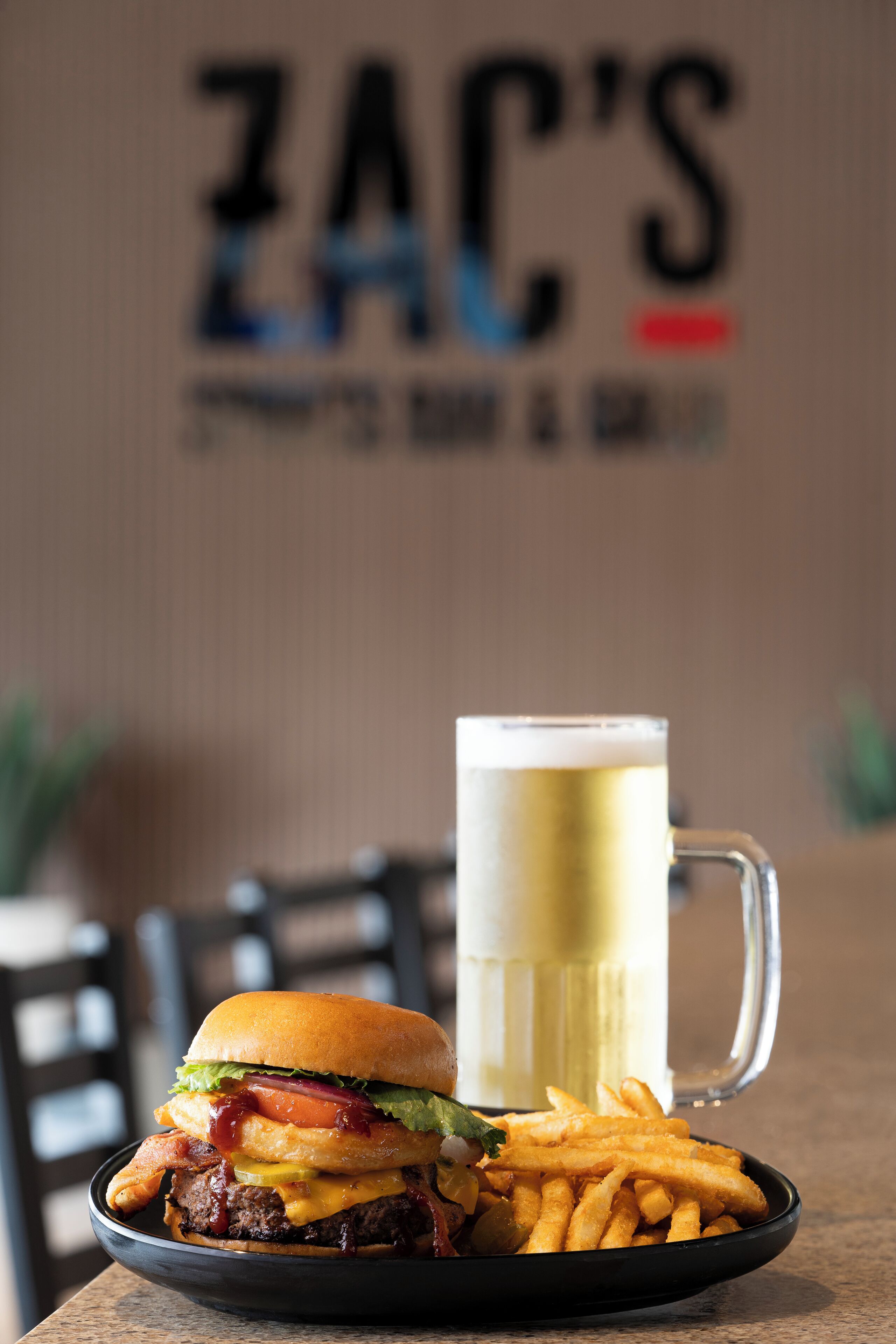 Una hamburguesa y un vaso de cerveza sobre una mesa, con un letrero al fondo.