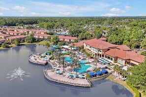 A resort with a large central pool, multiple guest villas, and a scenic view of the surrounding landscape.