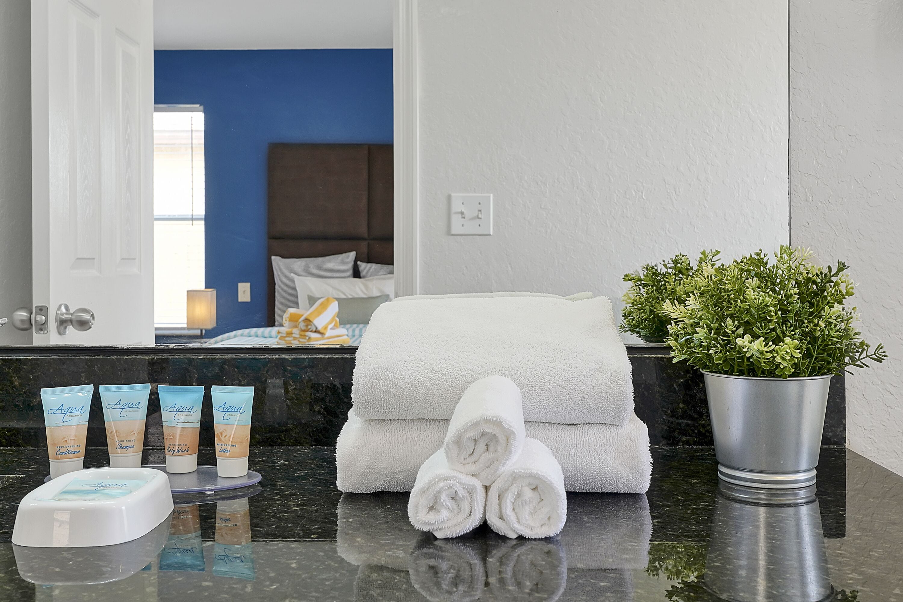 A bathroom with a blue wall, a white towel, a potted plant, and toiletries on the counter.