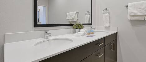 A bathroom with a white sink, dark cabinets, a large mirror, and a potted plant.