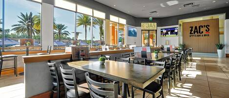 A spacious restaurant with large windows, a counter, and multiple tables and chairs.