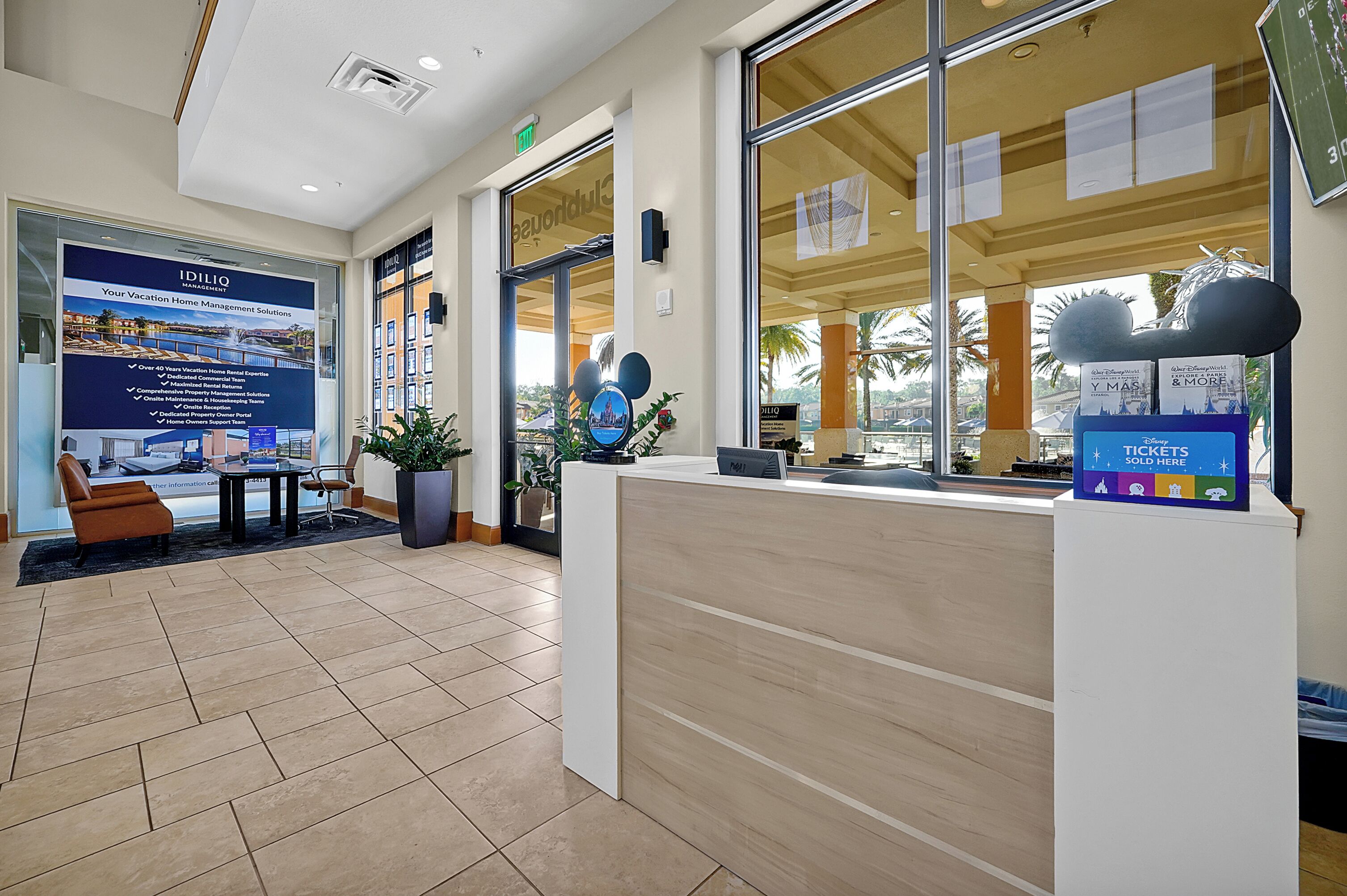 A reception area with a wooden reception desk, a seating area with a brown chair, and a large poster advertising vacation home management solutions.