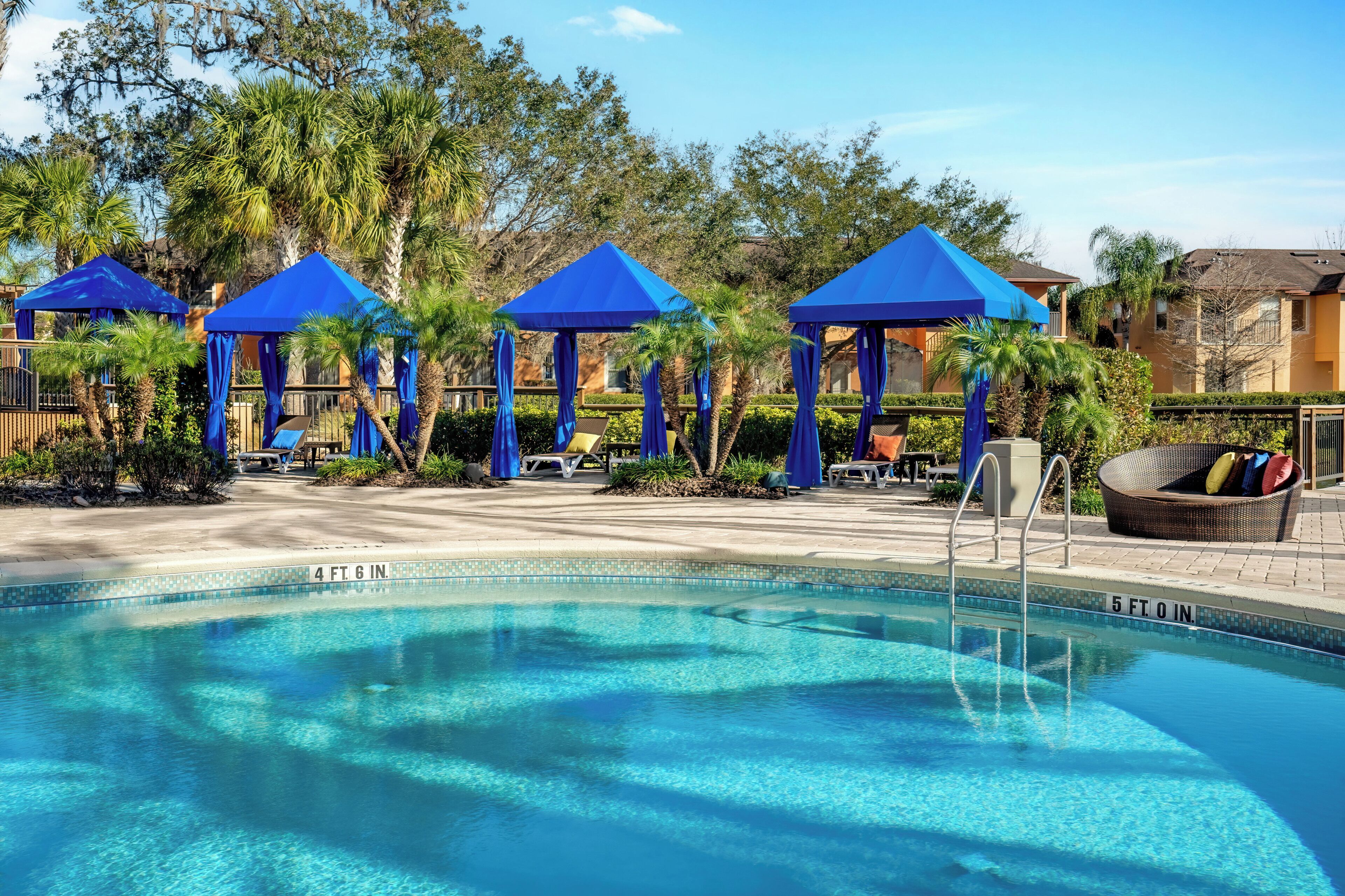 Une piscine dotée de parasols bleus, de chaises longues et surplombée d’un ciel d’un bleu limpide.