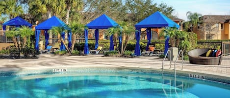 Une piscine dotée de parasols bleus, de chaises longues et surplombée d’un ciel d’un bleu limpide.