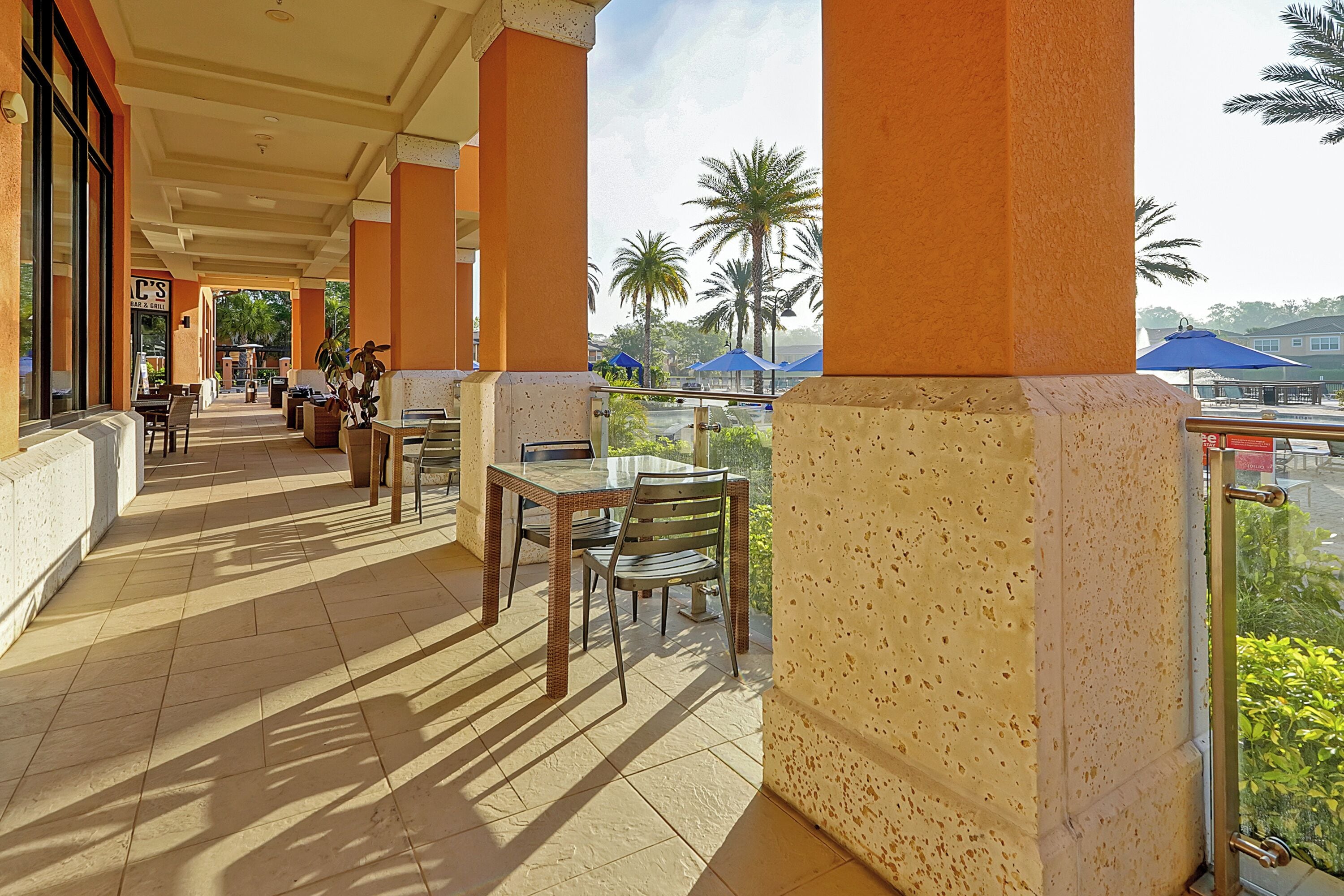 A covered outdoor area with tables and chairs, palm trees, and a view of the street.