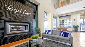 A lobby with a seating area featuring a sofa and a glass table, a potted plant, and a wall-mounted display.